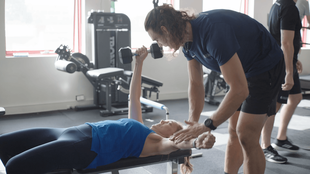 A State of Fitness coach spotting a member through a dumbbell press in the bright South Yarra studio.