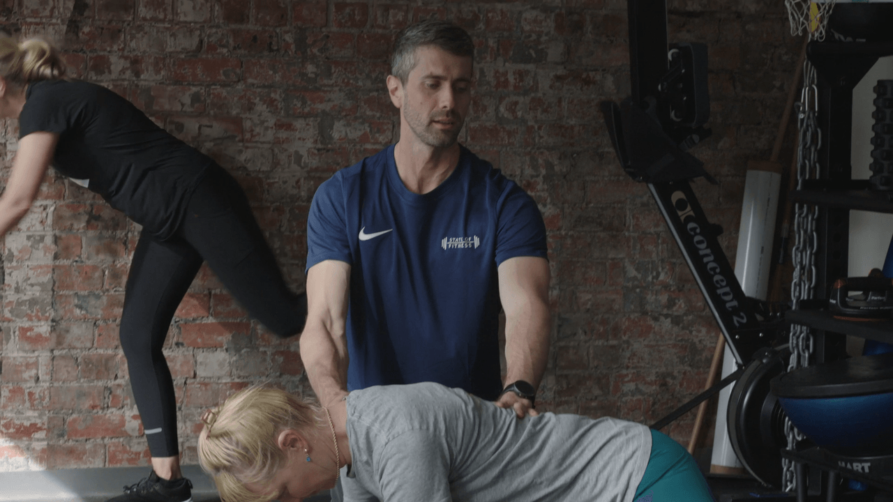A State of Fitness coach guiding a member through a hip hinge with hands-on technique cues.