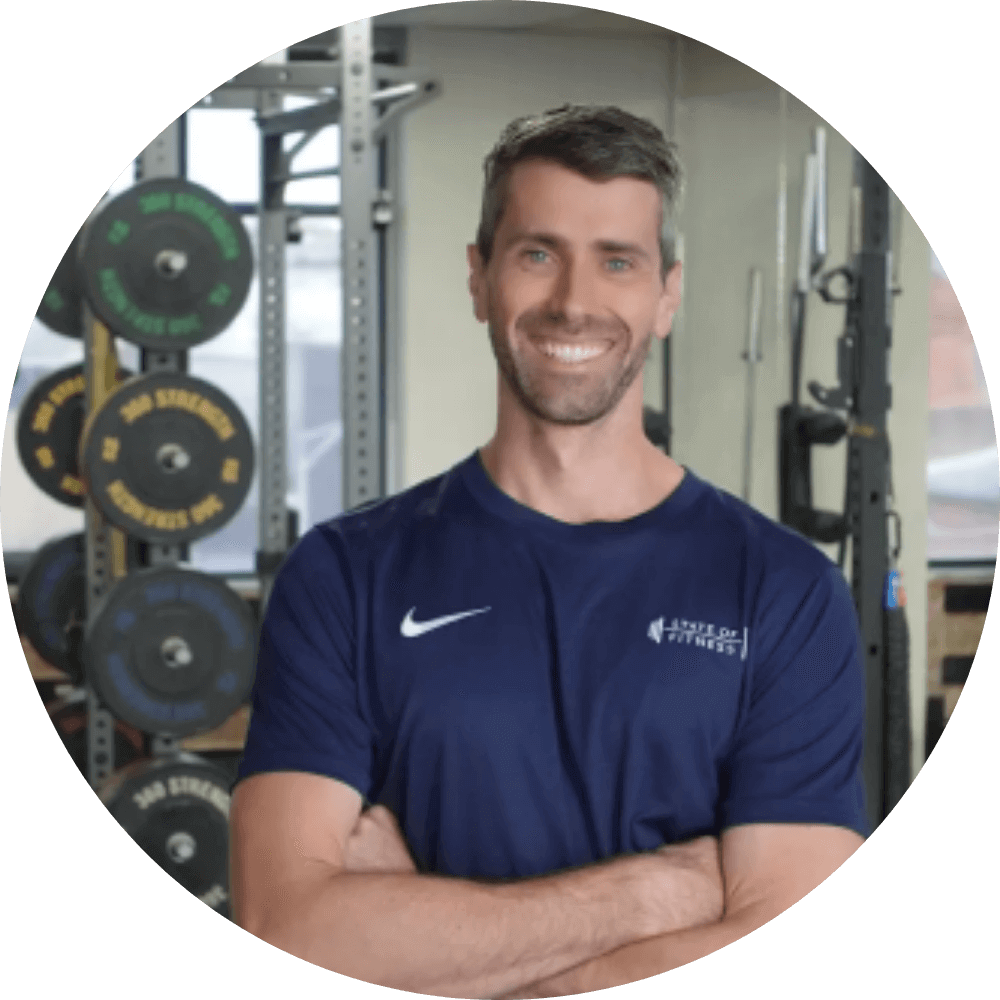 A man wearing a blue shirt poses against a backdrop of gym equipment at the State of Fitness studio.