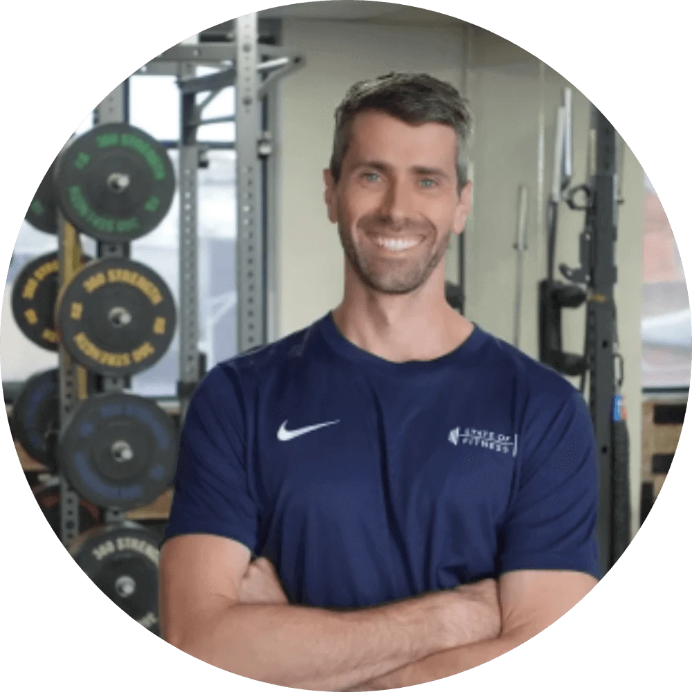 A man wearing a blue shirt poses against a backdrop of gym equipment at the State of Fitness studio.