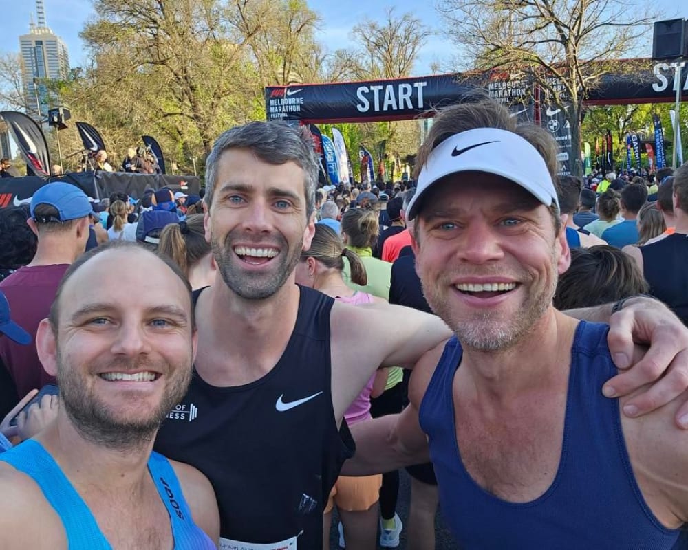 Three smiling men pose for the camera at a race, perfectly capturing a moment of joy and friendship.