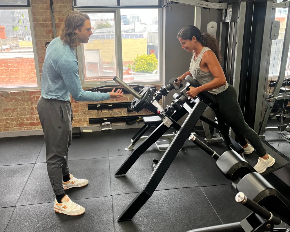 A personal trainer gives instructions to a woman as she engages in a fitness routine.
