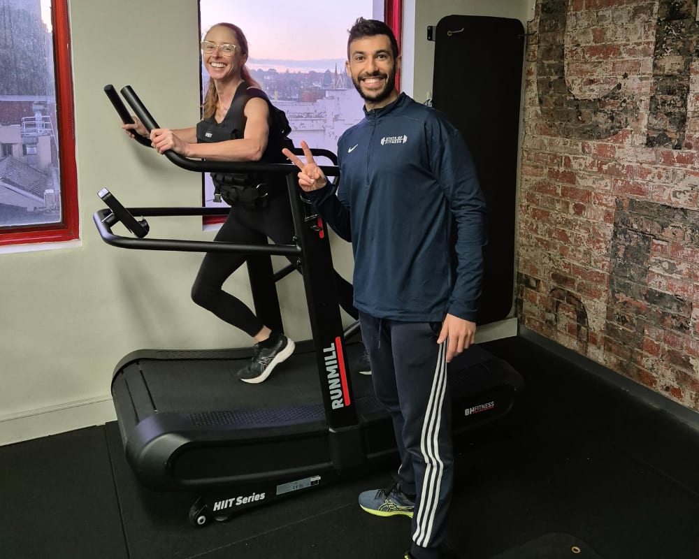 A woman on a treadmill and a man with a window showing a beautiful view, sunlight is beaming in, illuminating the space.