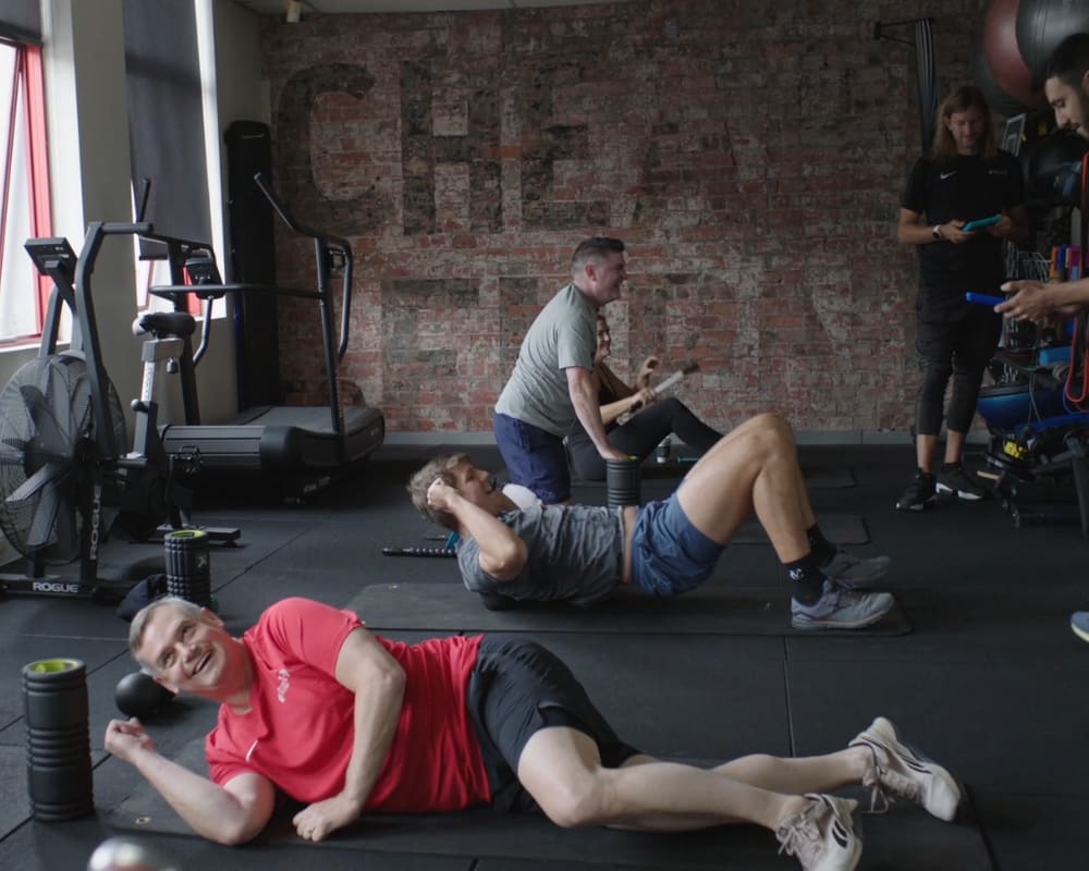 A group of people performing different exercises under the supervision of personal trainers, highlighting a dynamic and active fitness atmosphere.