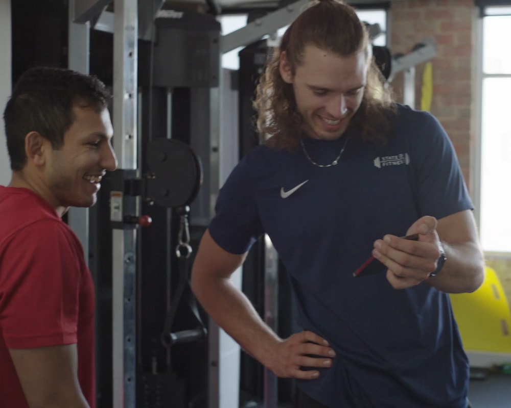 Two men in gym attire are looking at a cell phone together in a personal training studio.