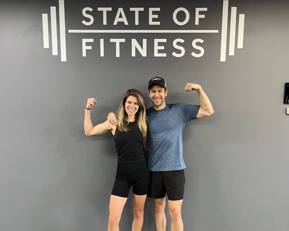 Personal coaches stand happily in front of a "State of Fitness" sign, showing their dedication to an active lifestyle.